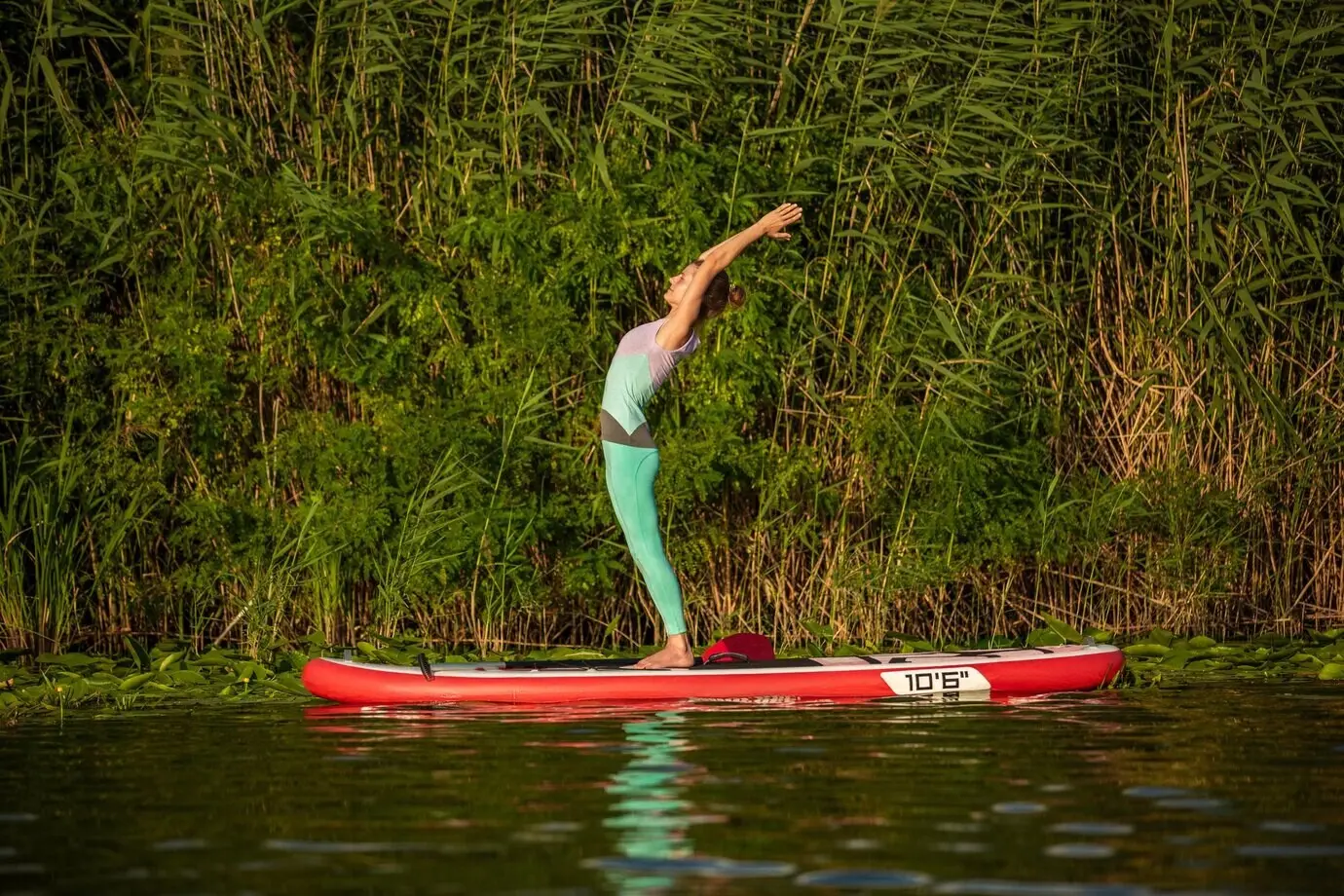 A young woman practices yoga on a stand-up paddleboard (SUP) on a beautiful lake or river. Healthy lifestyle concept. Sport. Yoga. Hobby.